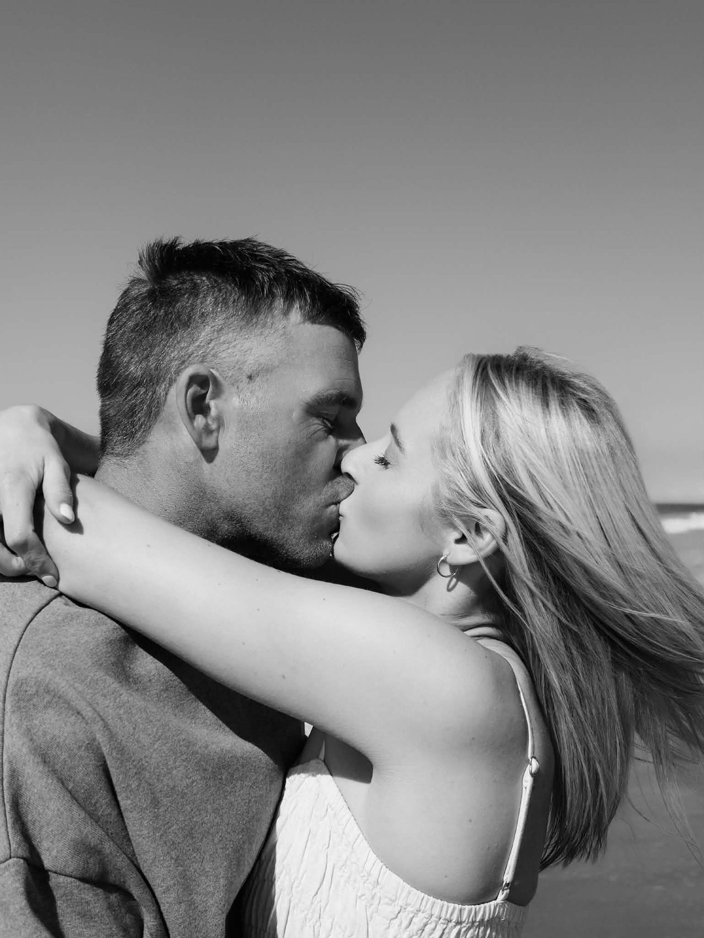 Black-and-white photograph of Lacy and Josh kissing by the sea