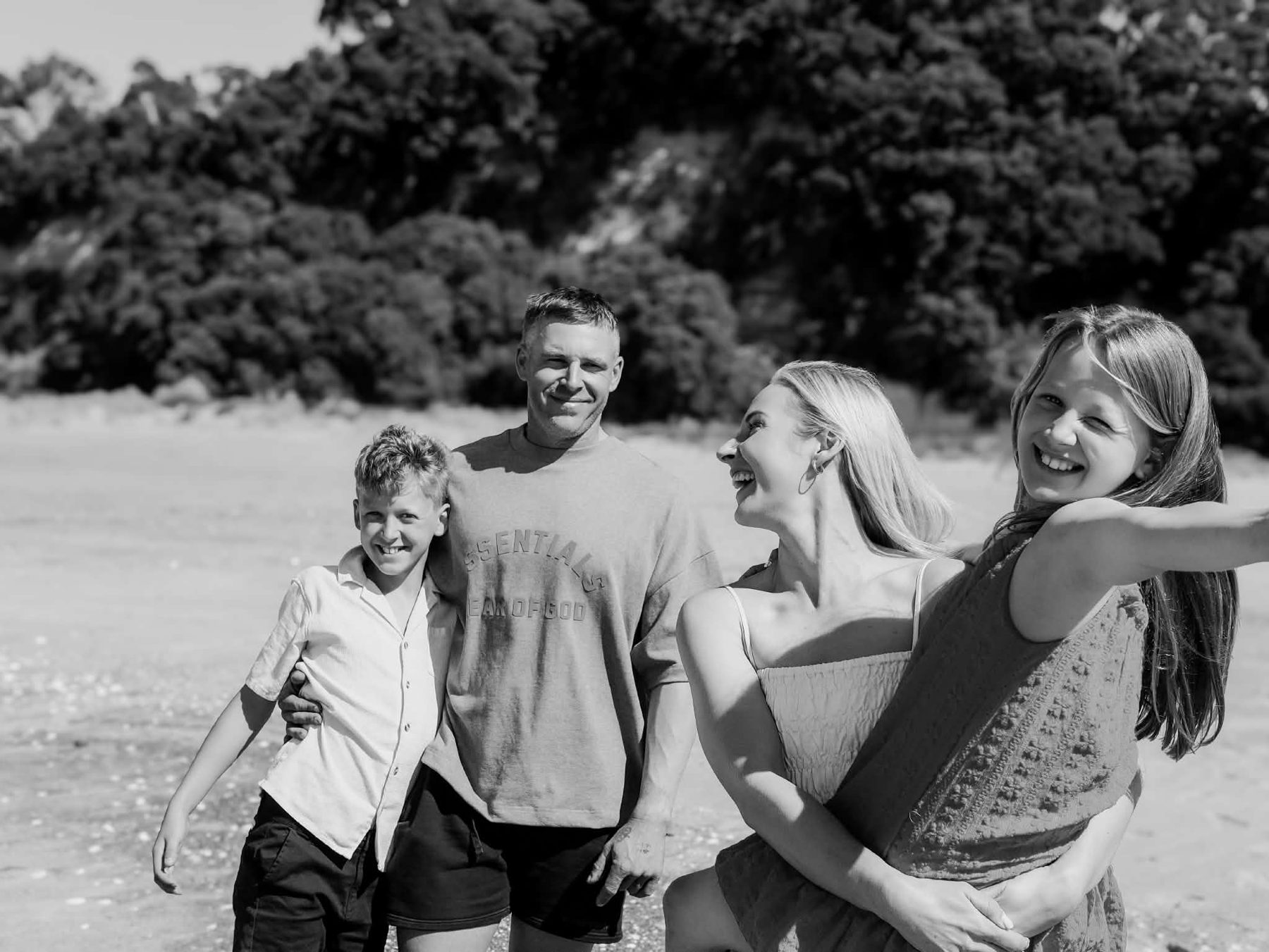 Black-and-white photograph of Lacy and Josh laughing on the beach with two young family members